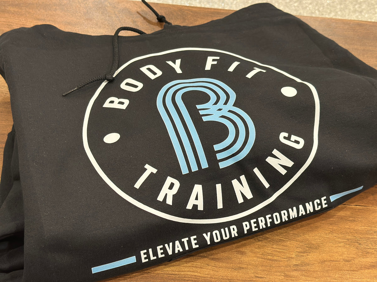 Stack of custom black hoodies featuring white and blue printed training logos, personalized by Cuart Studios in Spring, Texas.
