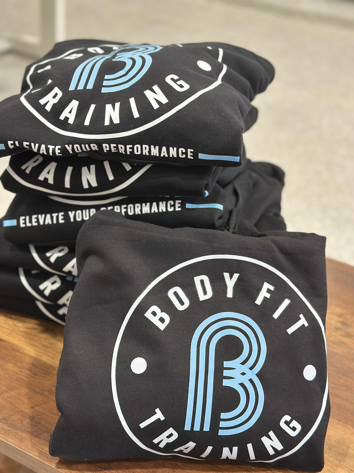 Stack of custom black hoodies featuring white and blue printed training logos, personalized by Cuart Studios in Spring, Texas.
